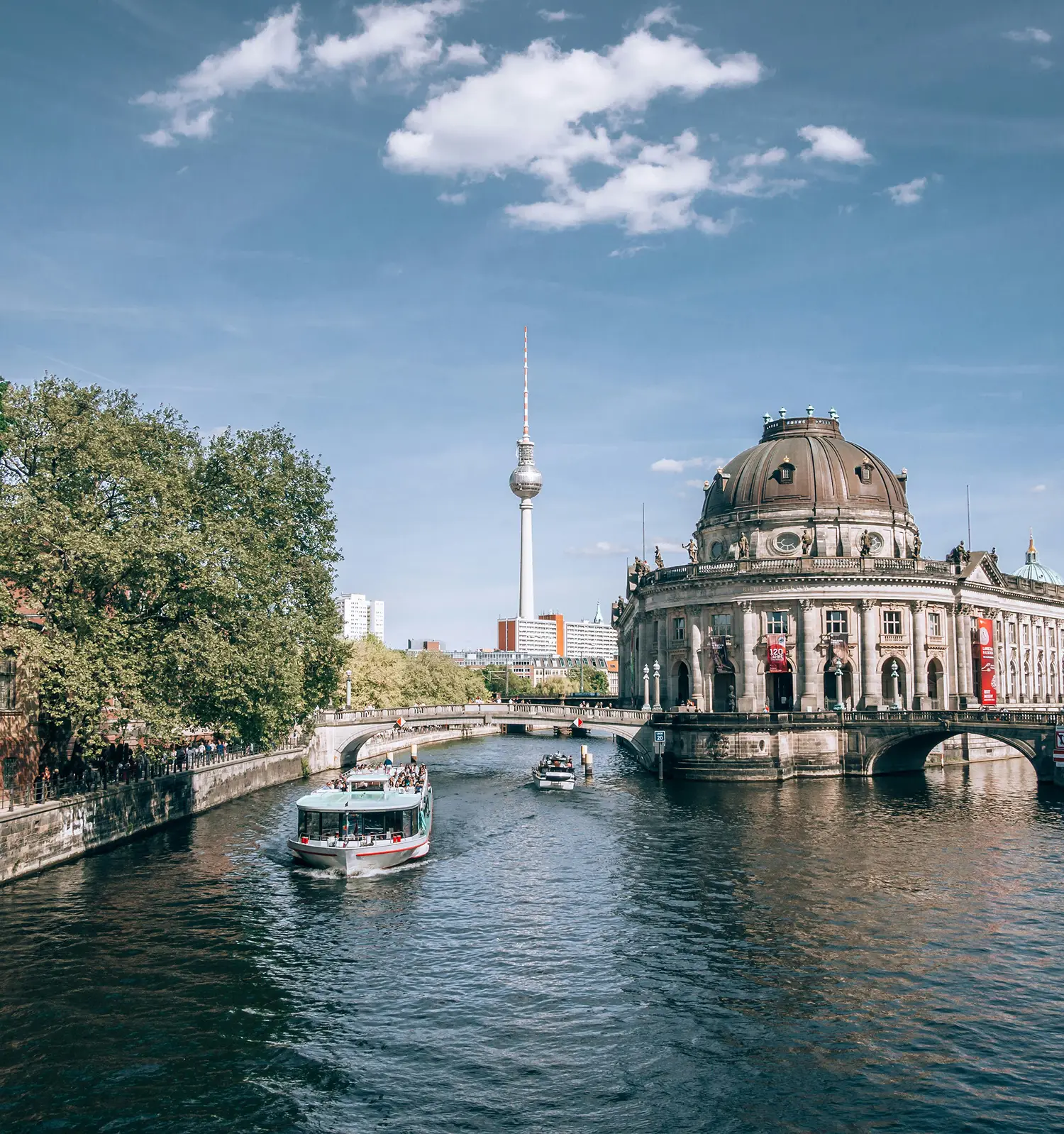 Das Bild zeigt eine malerische Stadtansicht von Berlin an einem sonnigen Tag mit blauem Himmel und vereinzelten weißen Wolken.