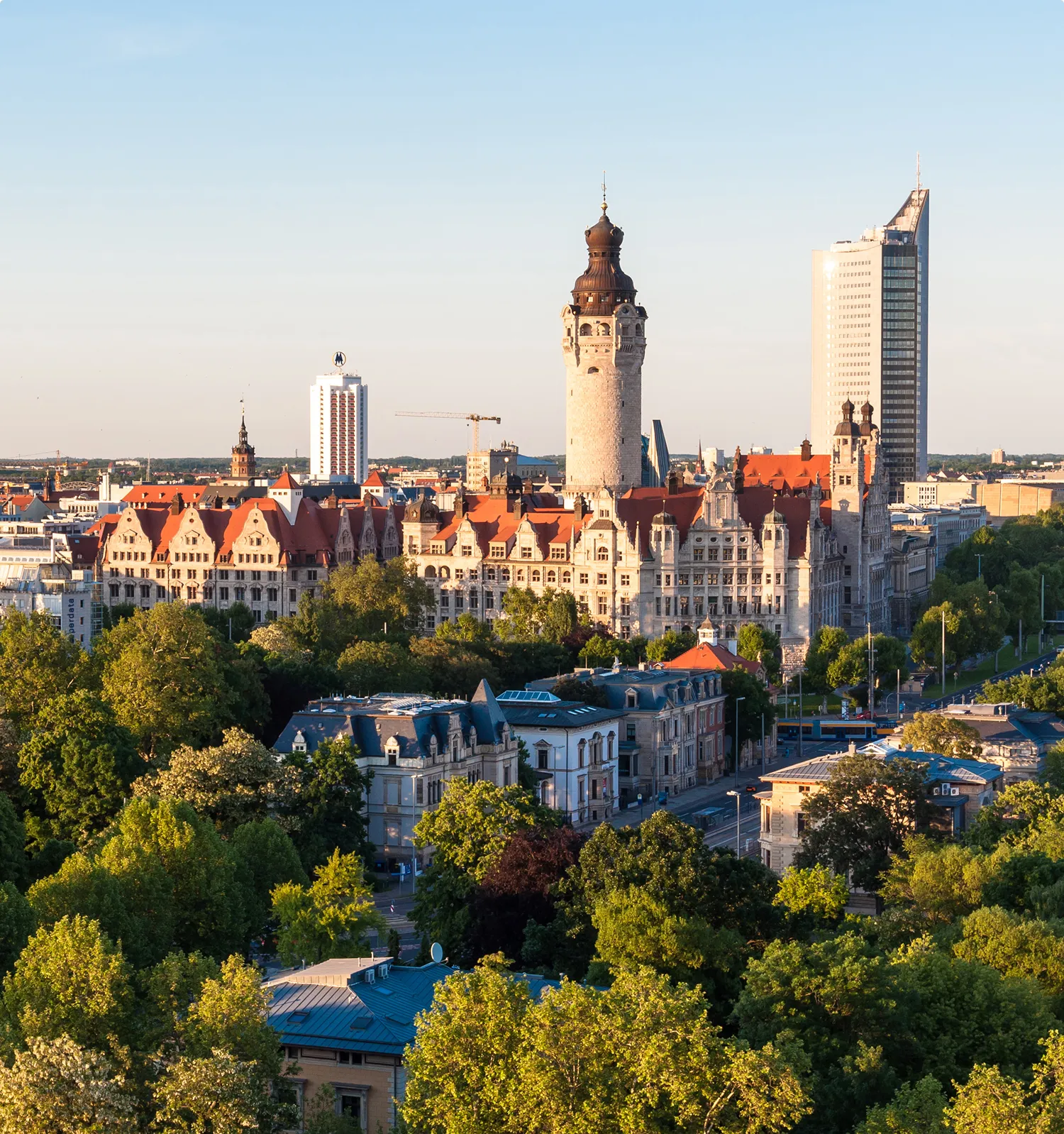 Stadtpanorama von Leipzig mit dem monumentalen Neuen Rathaus und seinem 115 Meter hohen Turm im Zentrum, umgeben von historischen Gründerzeitbauten und modernen Hochhäusern bei Abendlicht.
