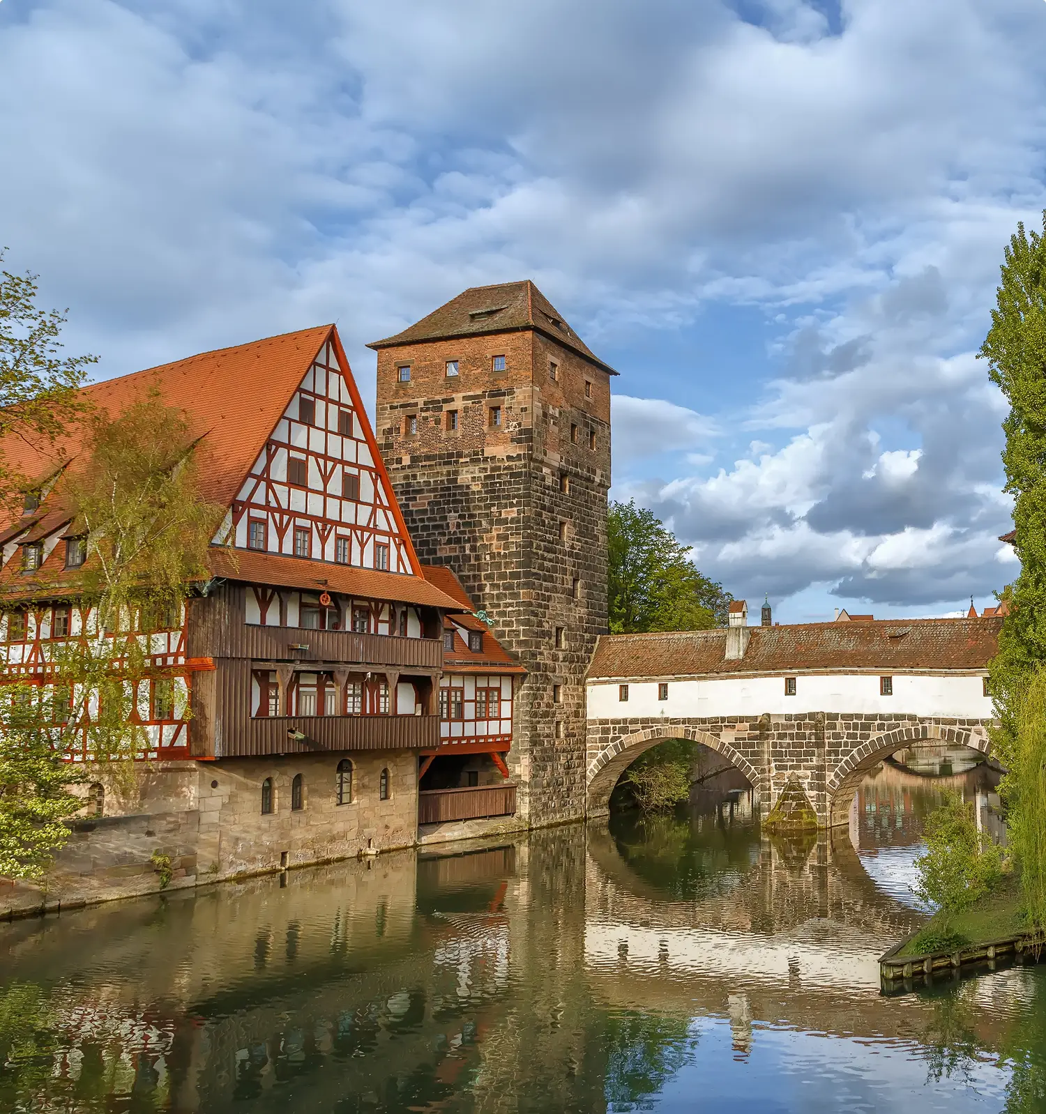 Historisches Nürnberger Weinstadel-Ensemble mit Fachwerkhaus und Henkerturm an der Pegnitz, verbunden durch die mittelalterliche Henkersteg-Brücke unter dramatischem Wolkenhimmel.