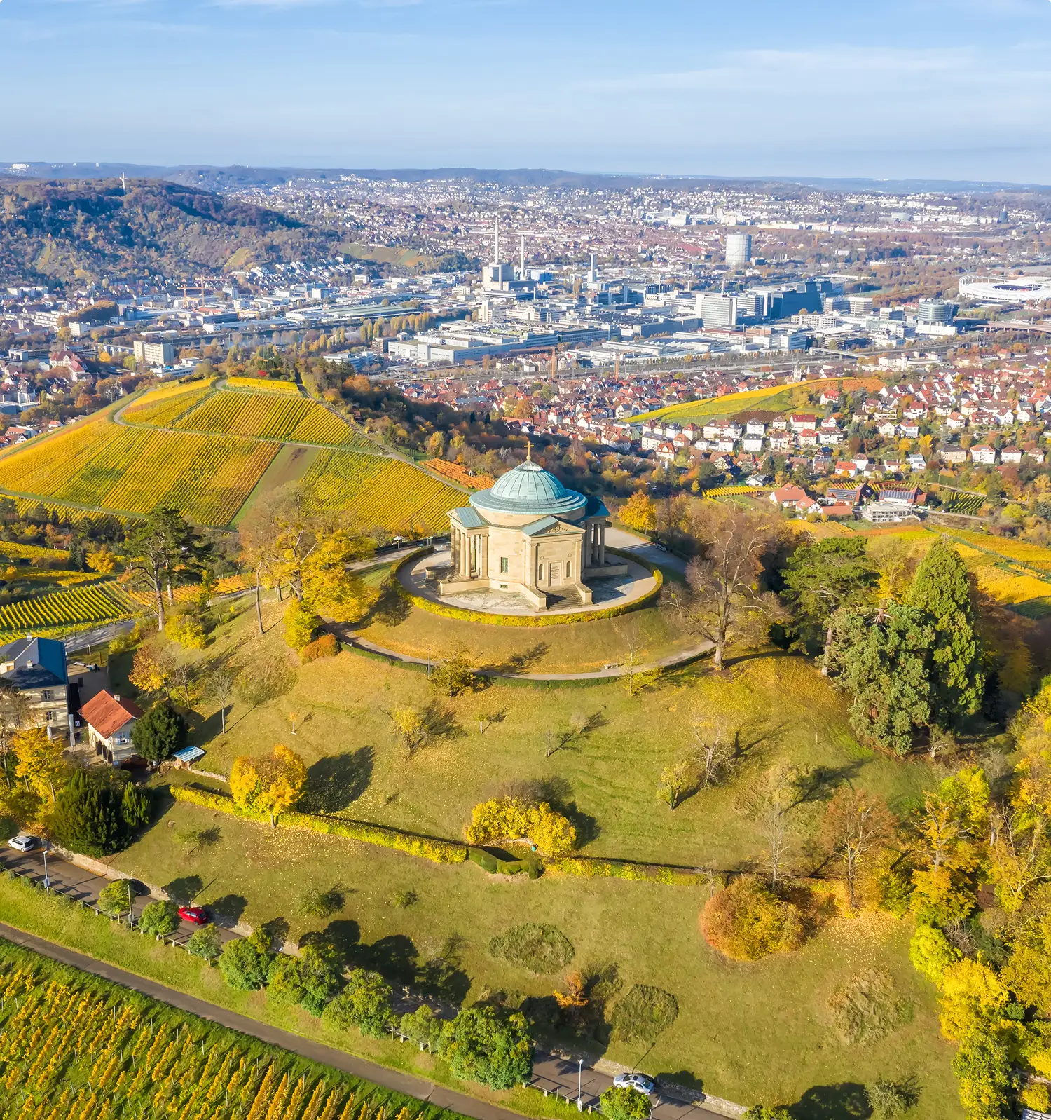 Herbstliche Luftaufnahme der Grabkapelle auf dem Württemberg mit klassizistischer Kuppelarchitektur, umgeben von goldgelben Weinbergen und Panoramablick auf Stuttgart im Hintergrund.