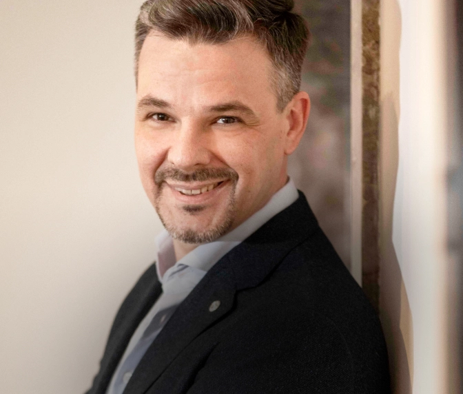 Markus Hauken - Professionelles Porträt eines lächelnden Mannes in dunklem Sakko und weißem Hemd vor neutralem Hintergrund.